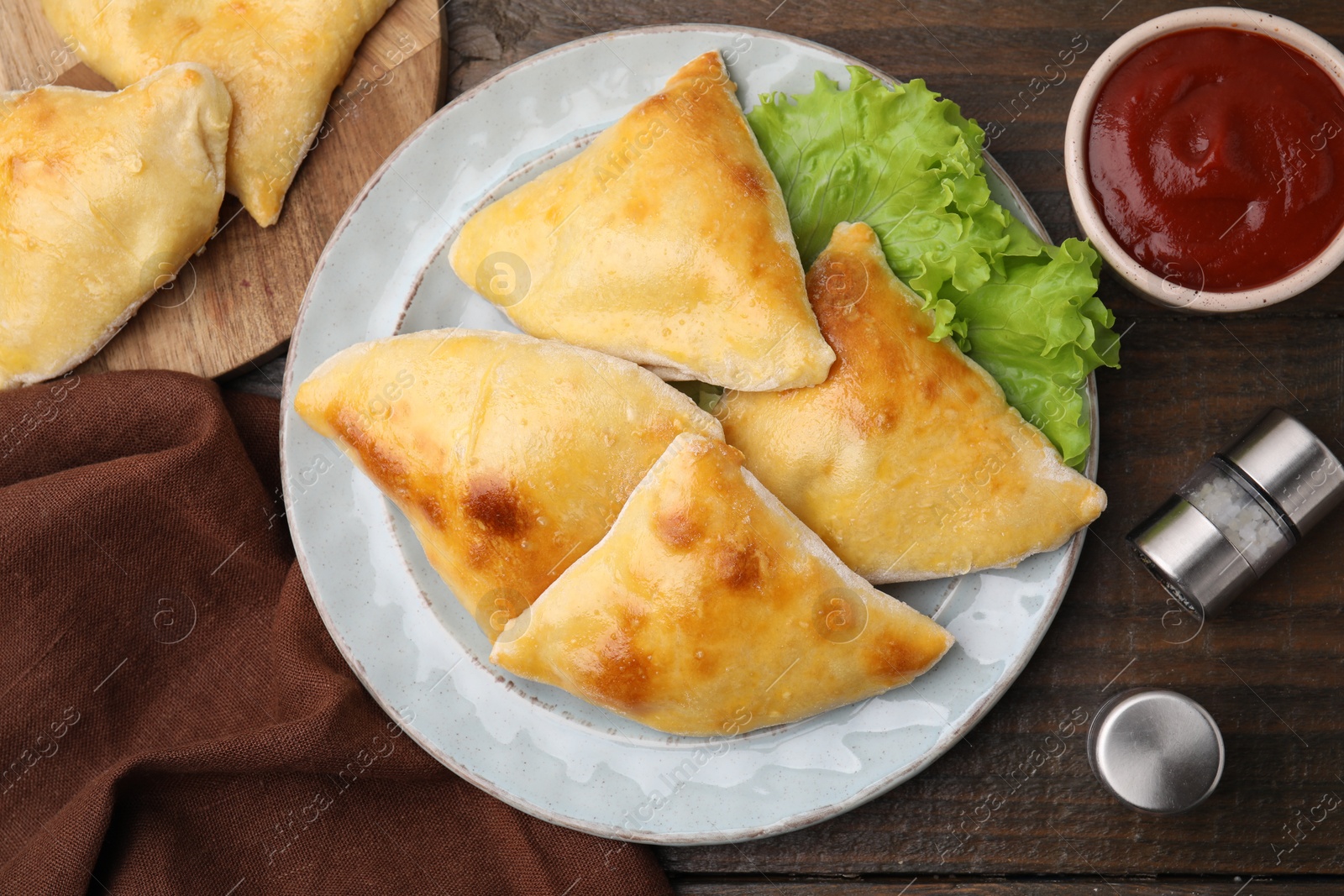 Photo of Delicious samosas with lettuce and tomato sauce on wooden table, flat lay