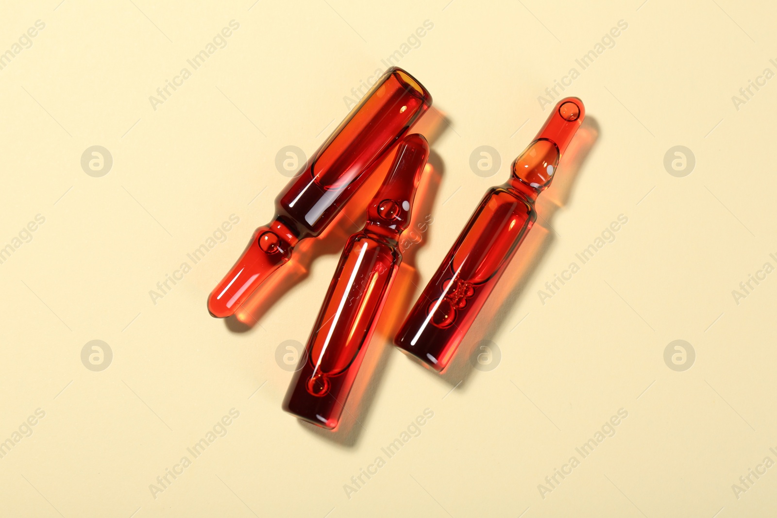 Photo of Glass ampoules with liquid on beige background, top view