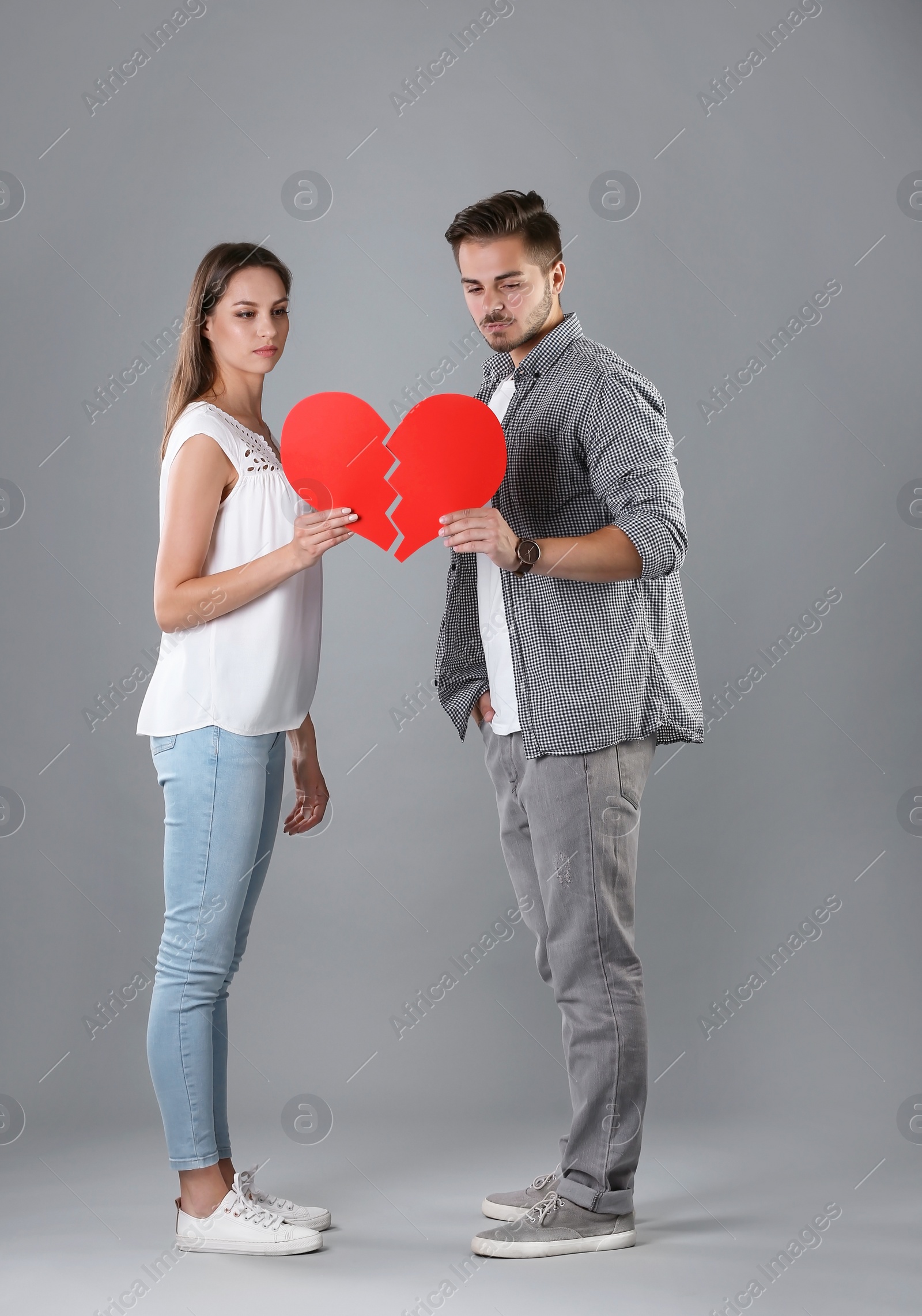 Photo of Young couple with torn paper heart on grey background. Relationship problems