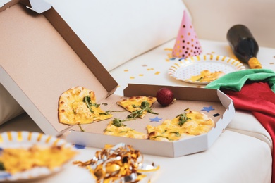 Photo of Pizza box with leftovers on sofa. Chaos after party