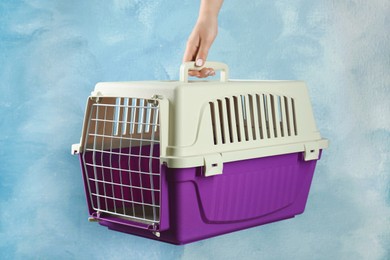 Photo of Woman holding violet pet carrier against light blue wall, closeup