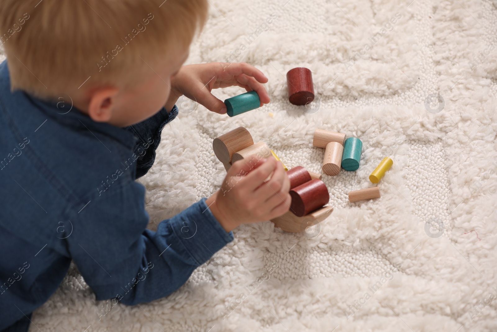 Photo of Little boy playing with wooden balance toy on carpet indoors, closeup