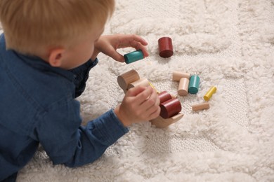 Photo of Little boy playing with wooden balance toy on carpet indoors, closeup