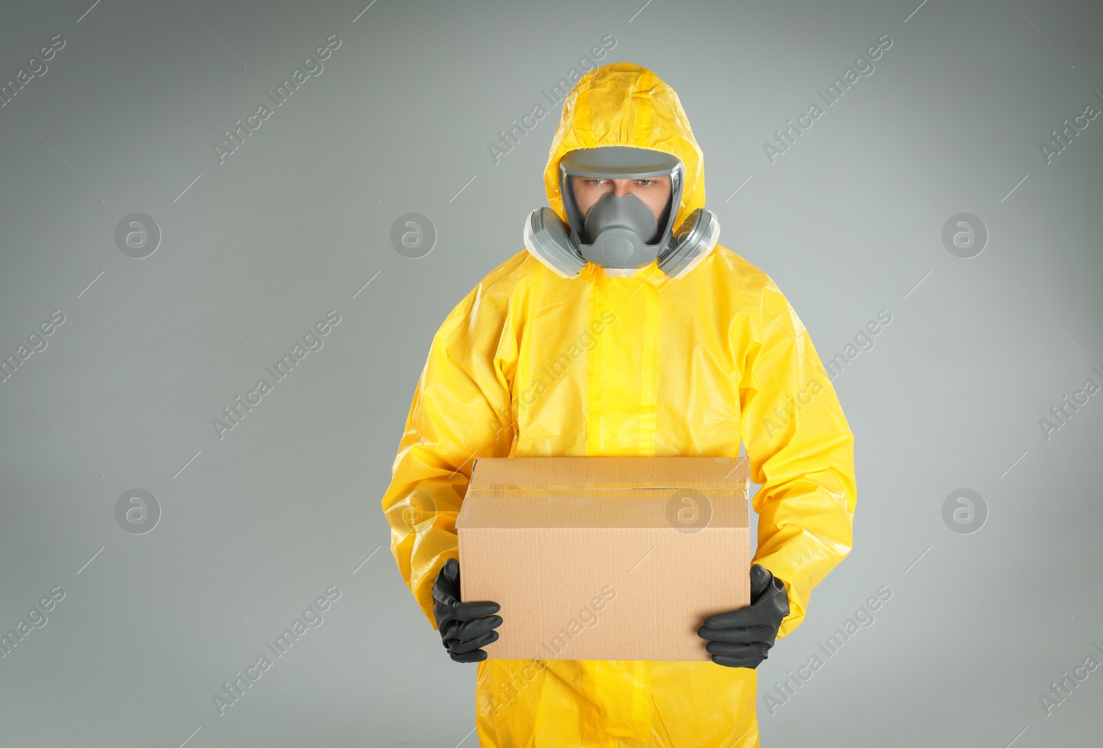 Photo of Man wearing chemical protective suit with cardboard box on light grey background. Prevention of virus spread