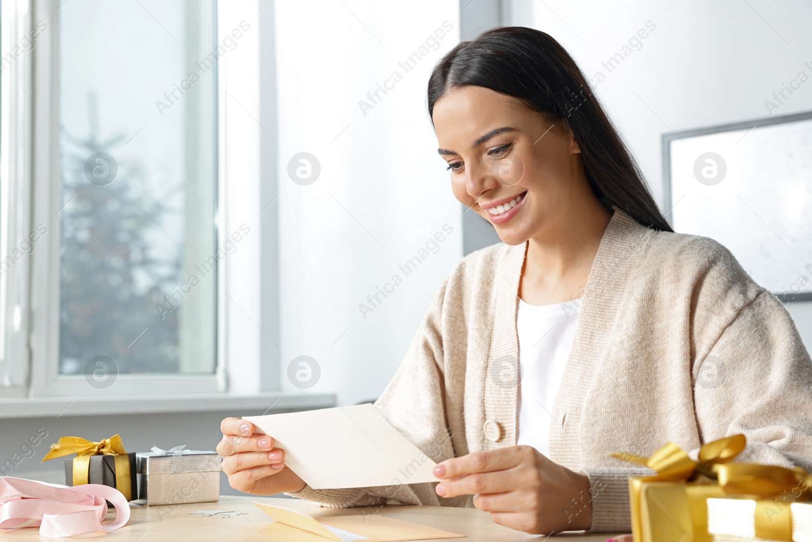 Photo of Happy woman reading greeting card at wooden table in room