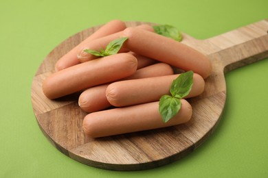 Photo of Delicious boiled sausages and basil on green table, closeup