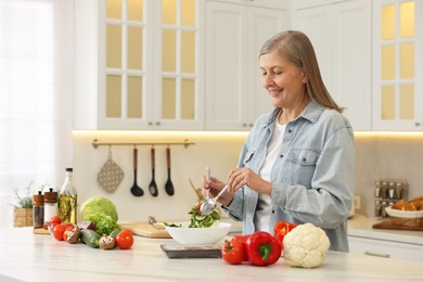 Happy woman making salad at table in kitchen