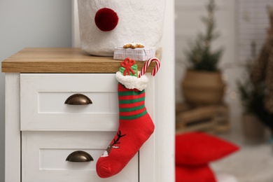 Photo of Stocking with presents hanging on drawer in children's room, space for text. Saint Nicholas Day tradition