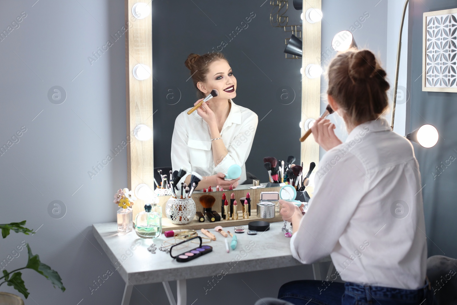 Photo of Beautiful young woman applying makeup in dressing room