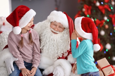 Photo of Little children sitting on authentic Santa Claus' knees indoors