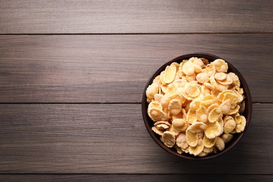 Photo of Bowl of tasty crispy corn flakes on wooden table, top view. Space for text