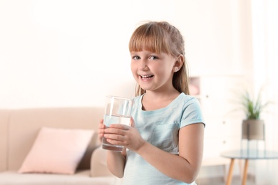 Cute little girl holding glass of fresh water at home