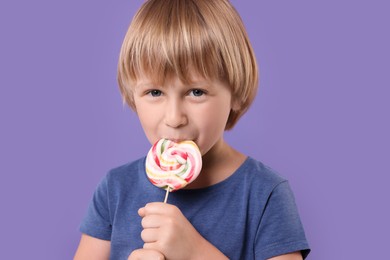 Photo of Happy little boy licking colorful lollipop swirl on violet background