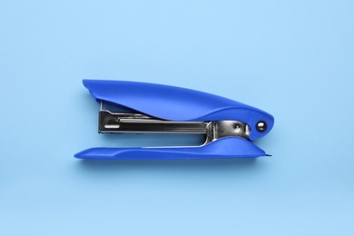 Photo of New bright stapler on light blue background, top view. School stationery