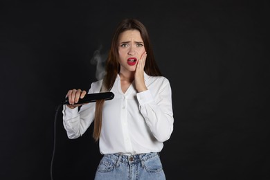Image of Stressed young woman with flattening iron on black background. Hair damage