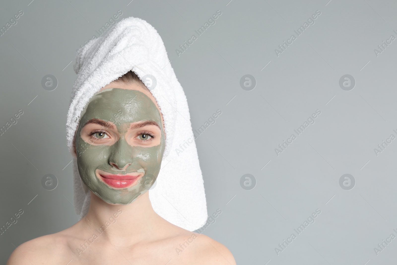 Photo of Young woman with clay mask on her face against grey background, space for text. Skin care