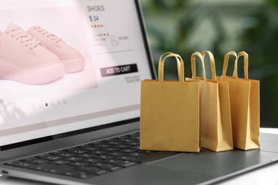 Photo of Online store. Small shopping bags on laptop, closeup