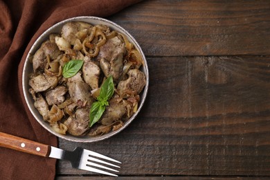 Photo of Delicious fried chicken liver with onion in bowl on wooden table, top view. Space for text