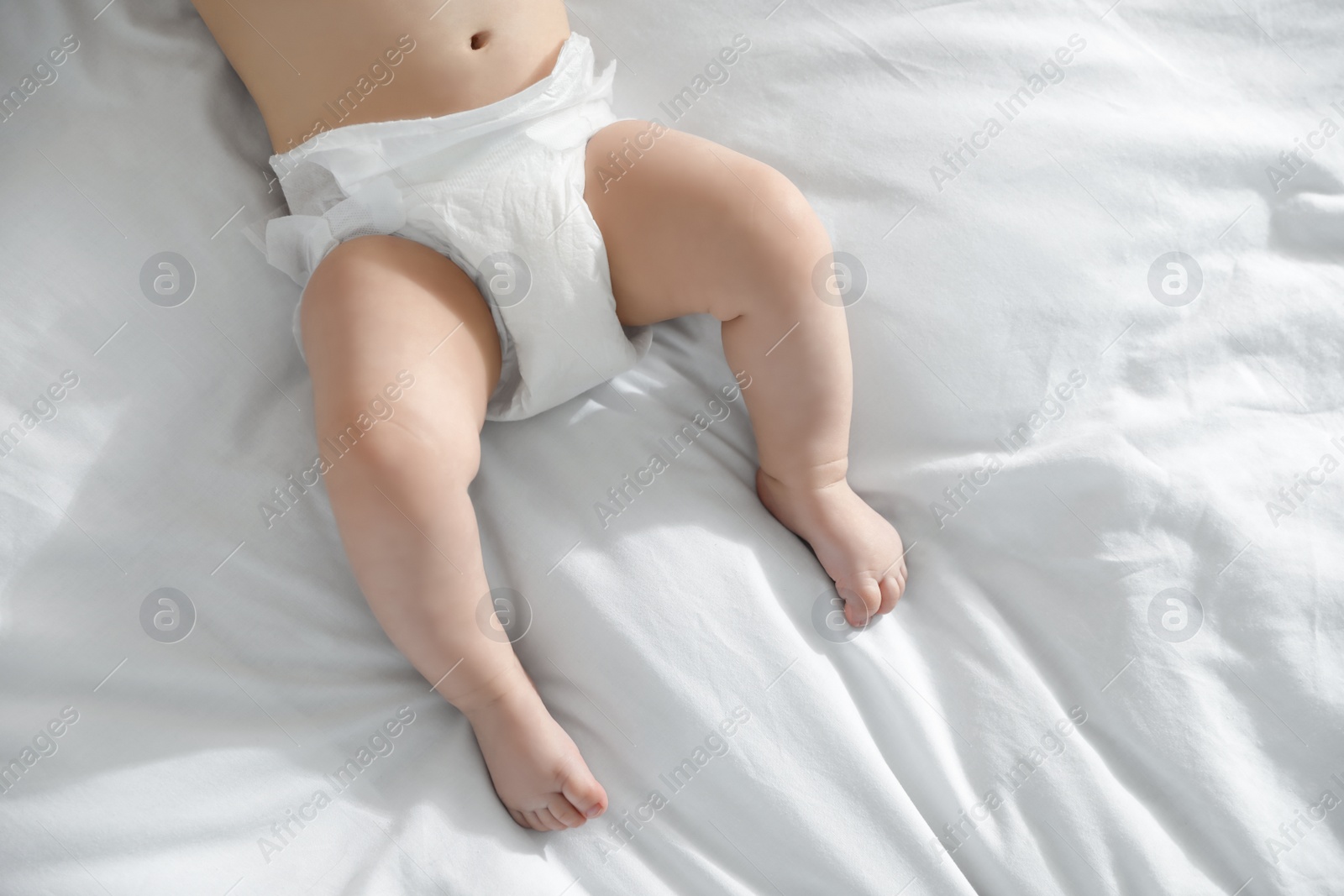 Photo of Little baby in diaper lying on bed at home, closeup view