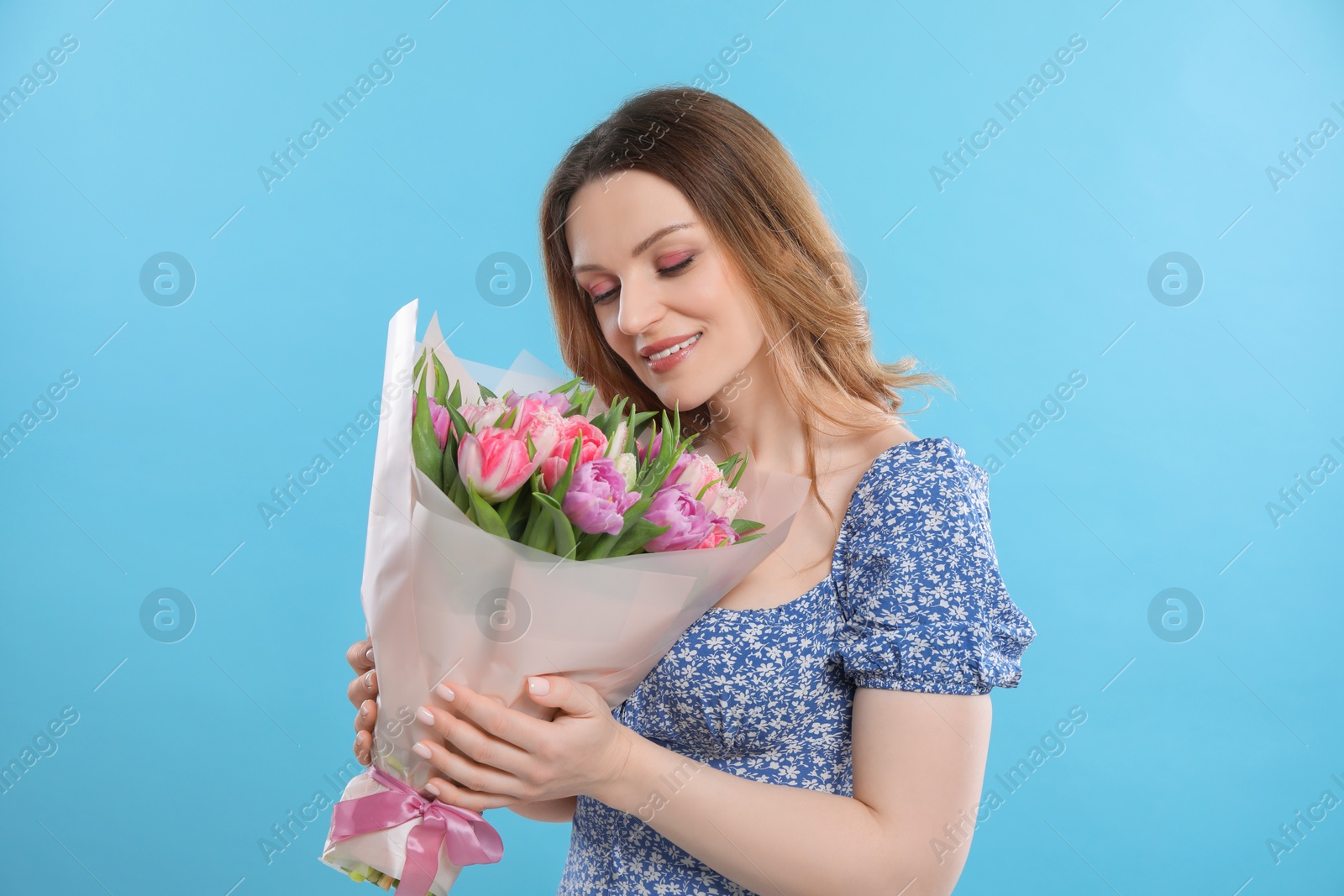 Photo of Happy young woman with bouquet of beautiful tulips on light blue background