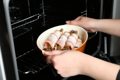 Photo of Woman putting ceramic baking dish with bacon wrapped asparagus in oven, closeup