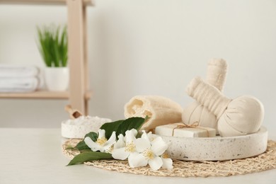 Photo of Beautiful jasmine flowers, herbal bags and soap bar on white wooden table indoors, space for text