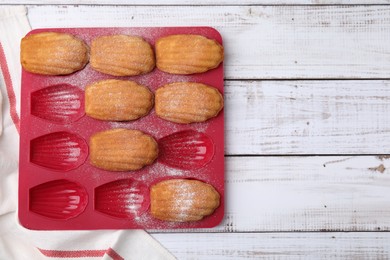 Photo of Delicious madeleine cookies in baking mold on white wooden table, top view. Space for text