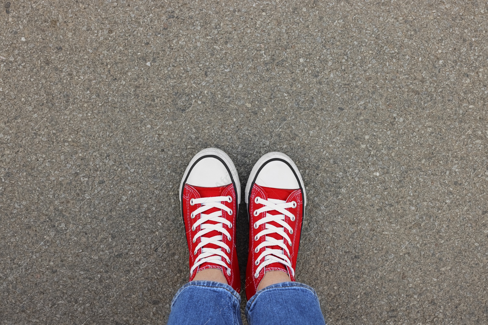 Photo of Woman in stylish gumshoes on asphalt, top view