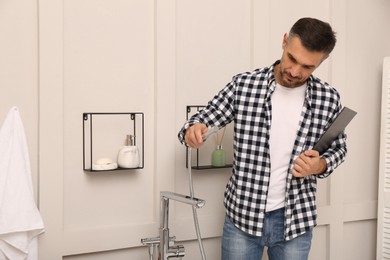 Plumber with clipboard checking water tap in bathroom