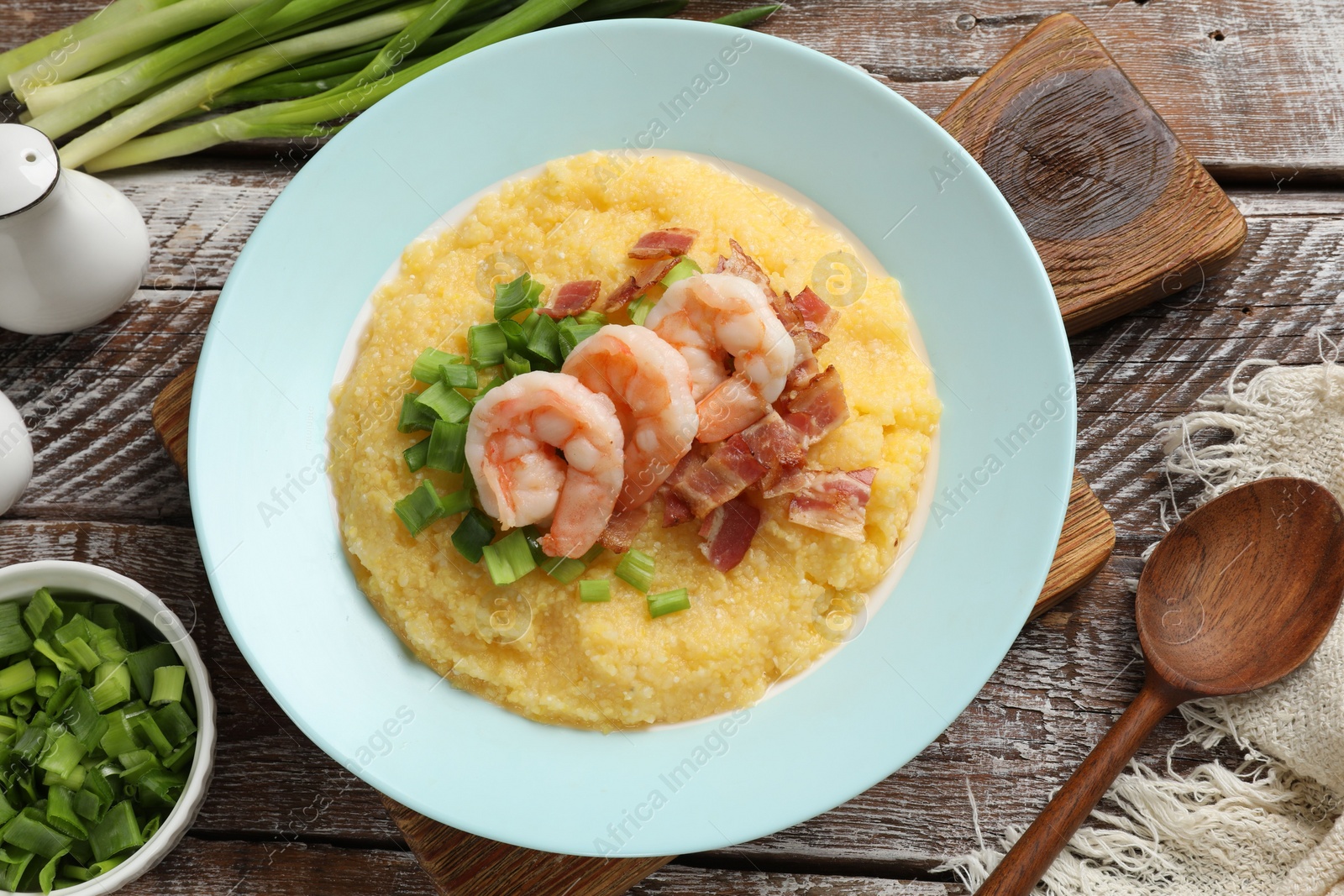 Photo of Plate with fresh tasty shrimps, bacon, grits and green onion on wooden table, flat lay