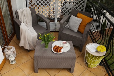 Different pillows, blanket, breakfast and beautiful tulips on rattan garden furniture outdoors