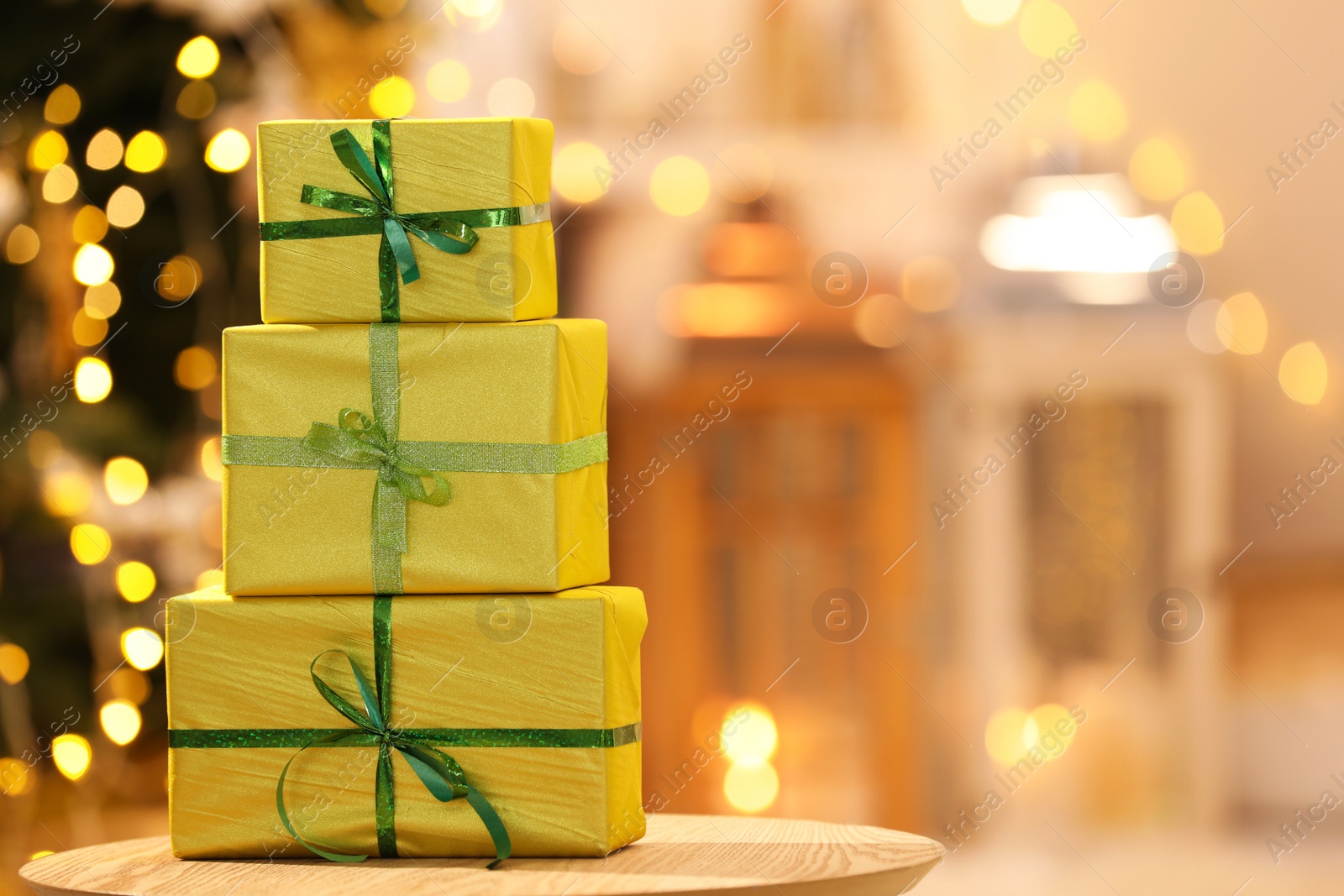 Photo of Beautifully wrapped gift boxes on wooden table against blurred festive lights, space for text. Christmas celebration