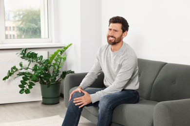 Photo of Man suffering from leg pain on sofa in room