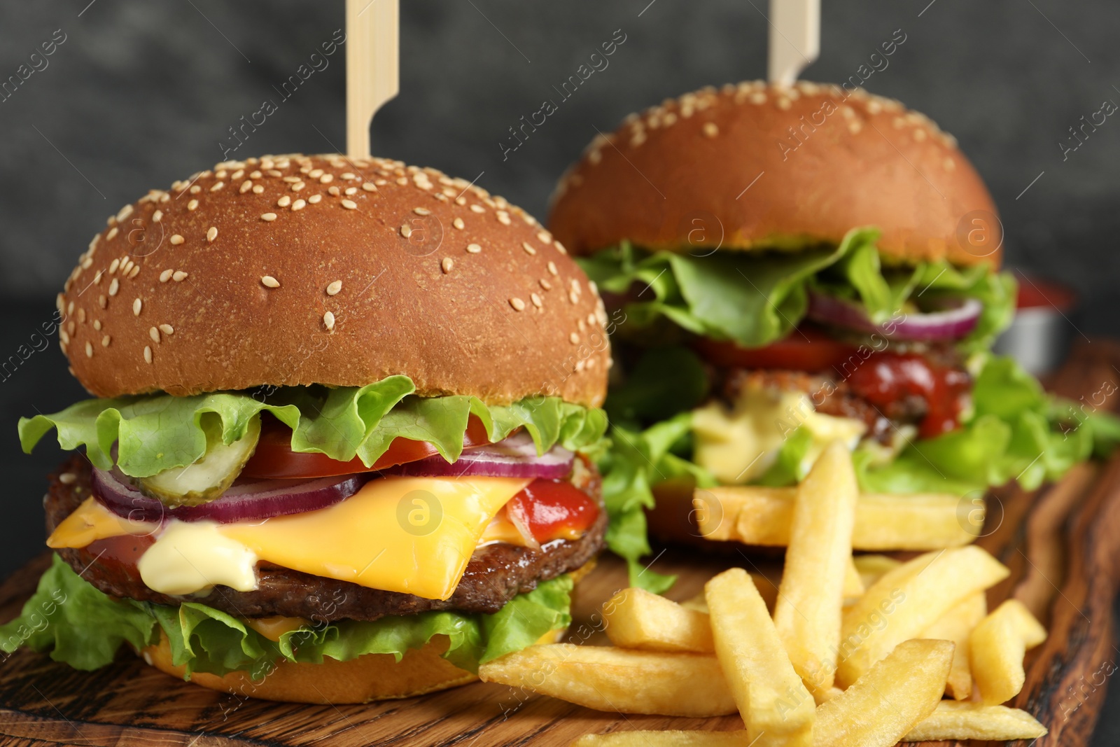 Photo of Delicious burgers with beef patty and french fries on wooden board, closeup