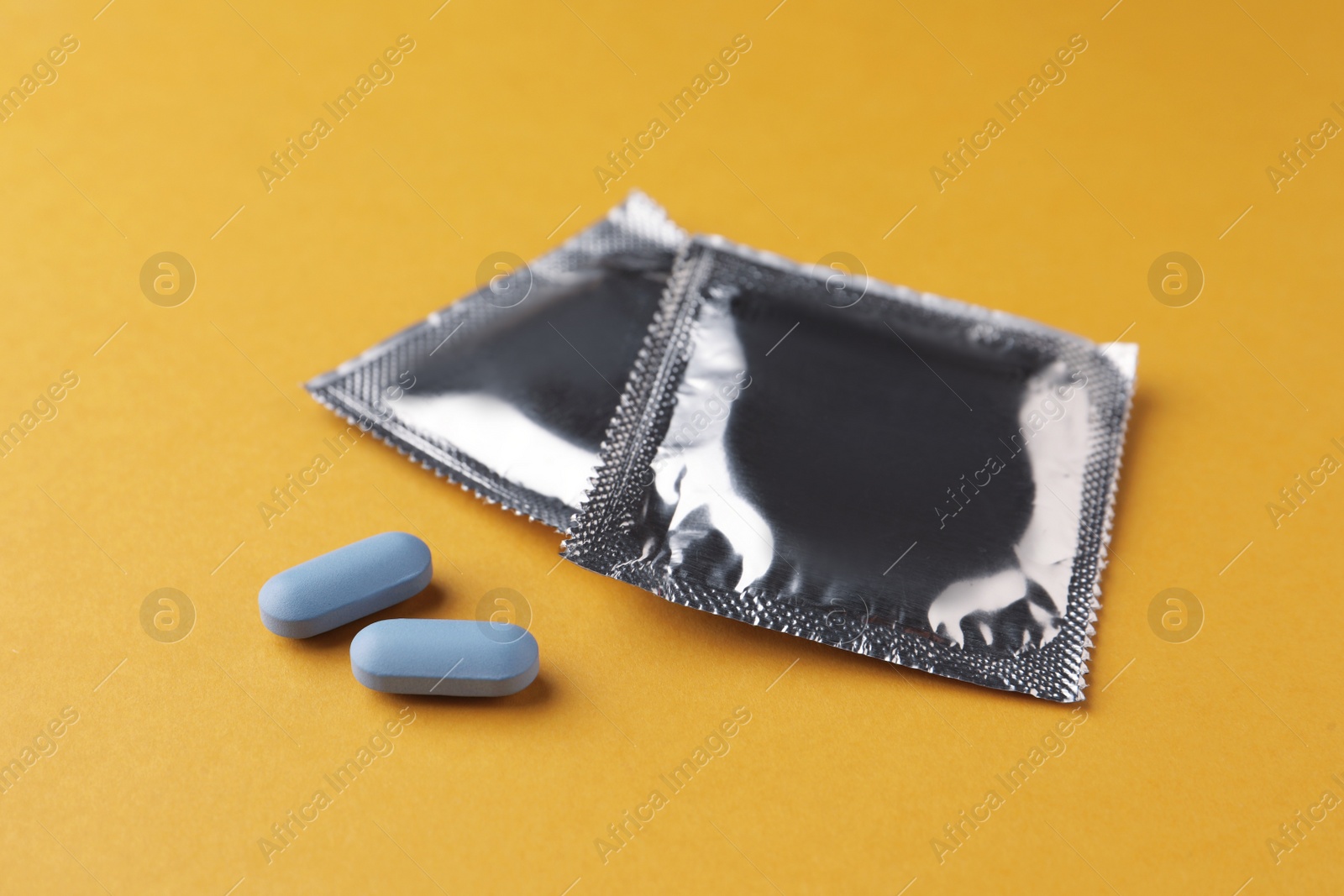 Photo of Pills and condoms on orange background. Potency problem