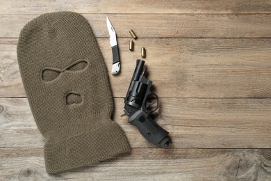 Flat lay composition with balaclava and weapons on wooden table, space for text