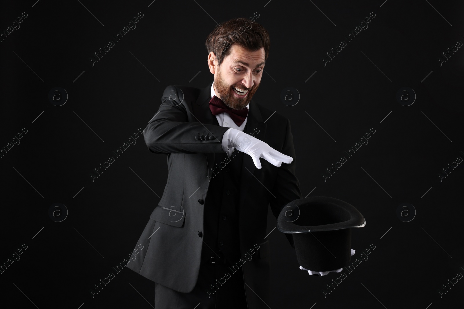 Photo of Happy magician showing magic trick with top hat on black background