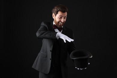 Photo of Happy magician showing magic trick with top hat on black background