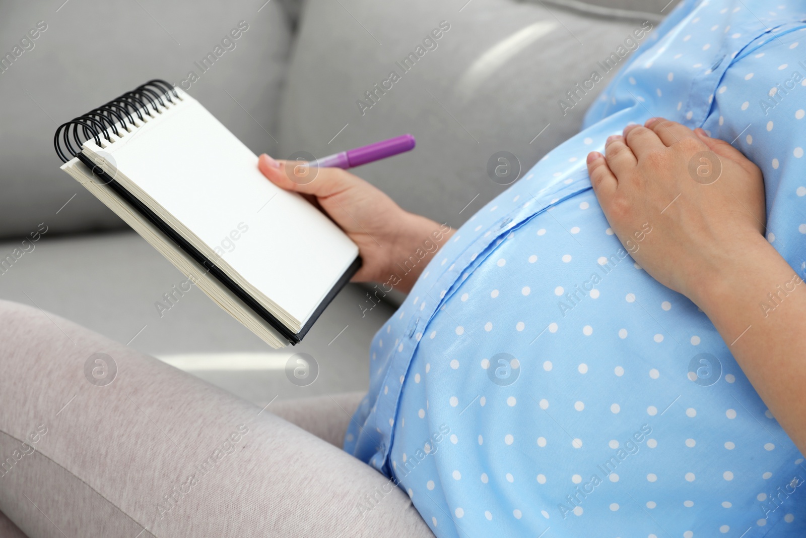 Photo of Pregnant woman with notebook and marker choosing name for baby on sofa, closeup