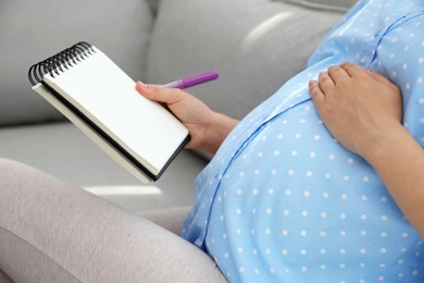 Photo of Pregnant woman with notebook and marker choosing name for baby on sofa, closeup