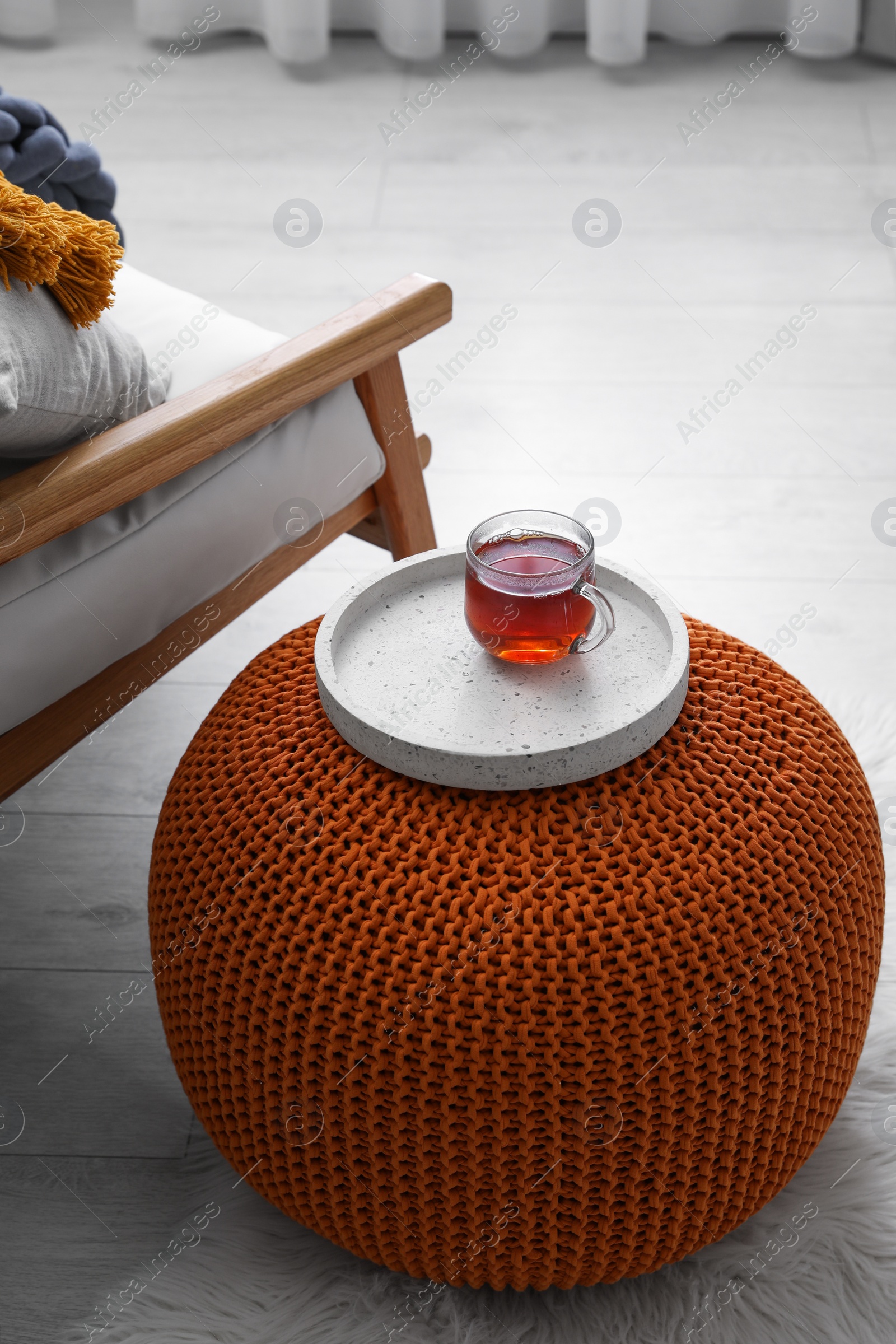 Photo of Tray with cup of tea on stylish knitted pouf in room. Interior design