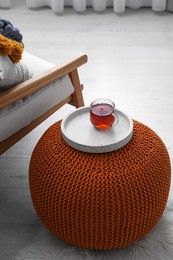 Photo of Tray with cup of tea on stylish knitted pouf in room. Interior design