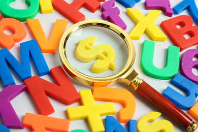 Photo of Magnifying glass over dollar sign surrounded by magnet letters on white background, closeup. Search concept