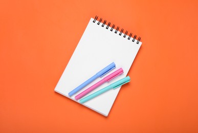 Photo of Blank office notebook and pens on orange background, top view