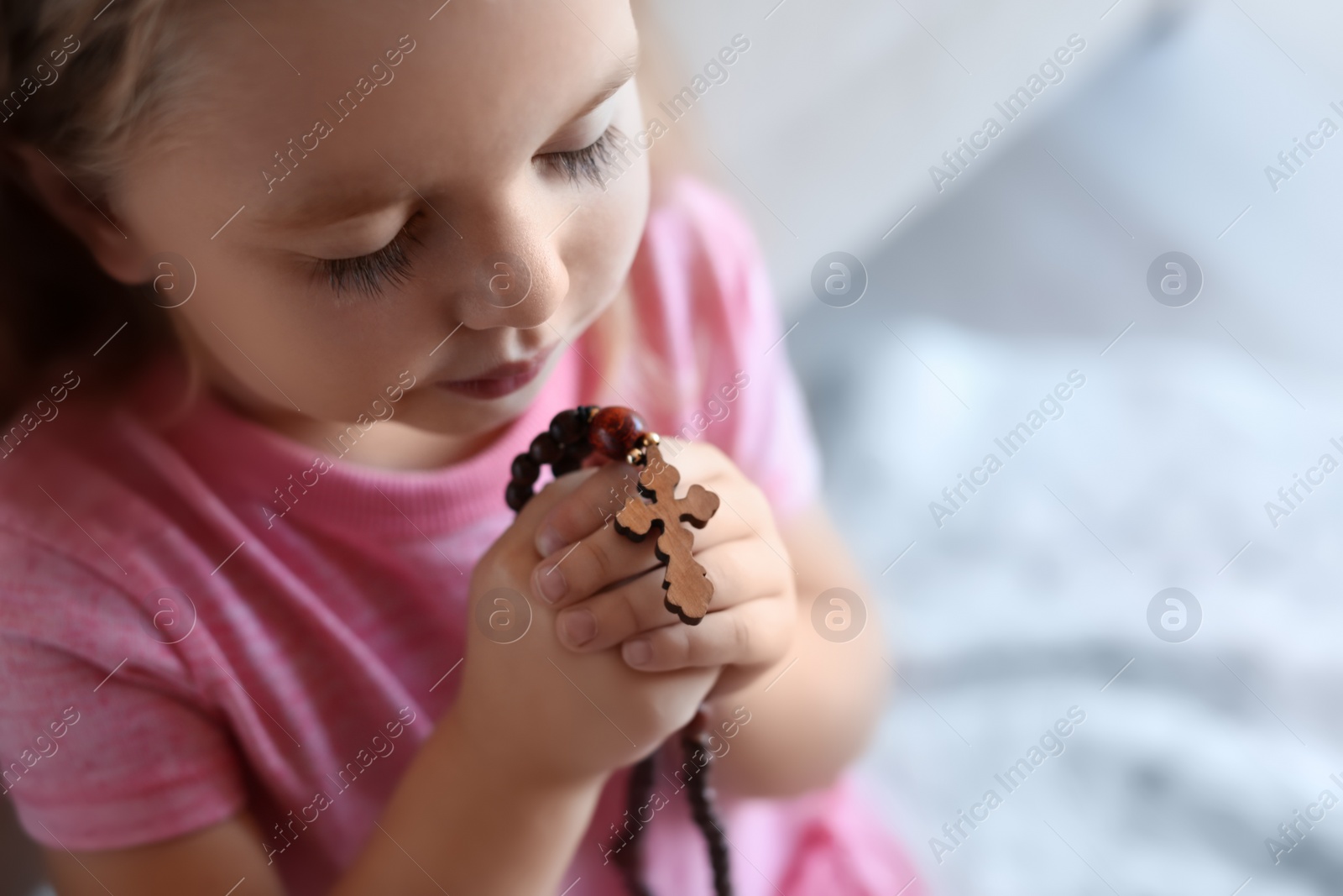 Photo of Cute little girl with beads praying on blurred background