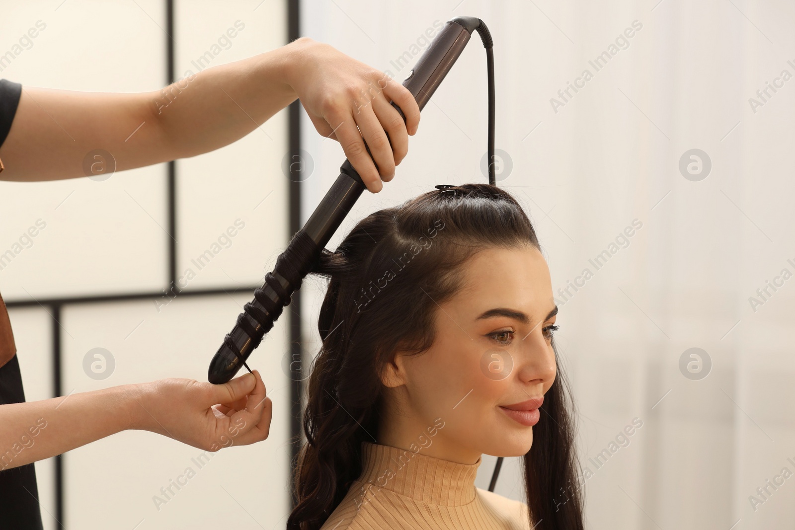 Photo of Hair styling. Hairdresser curling woman's hair in salon, closeup