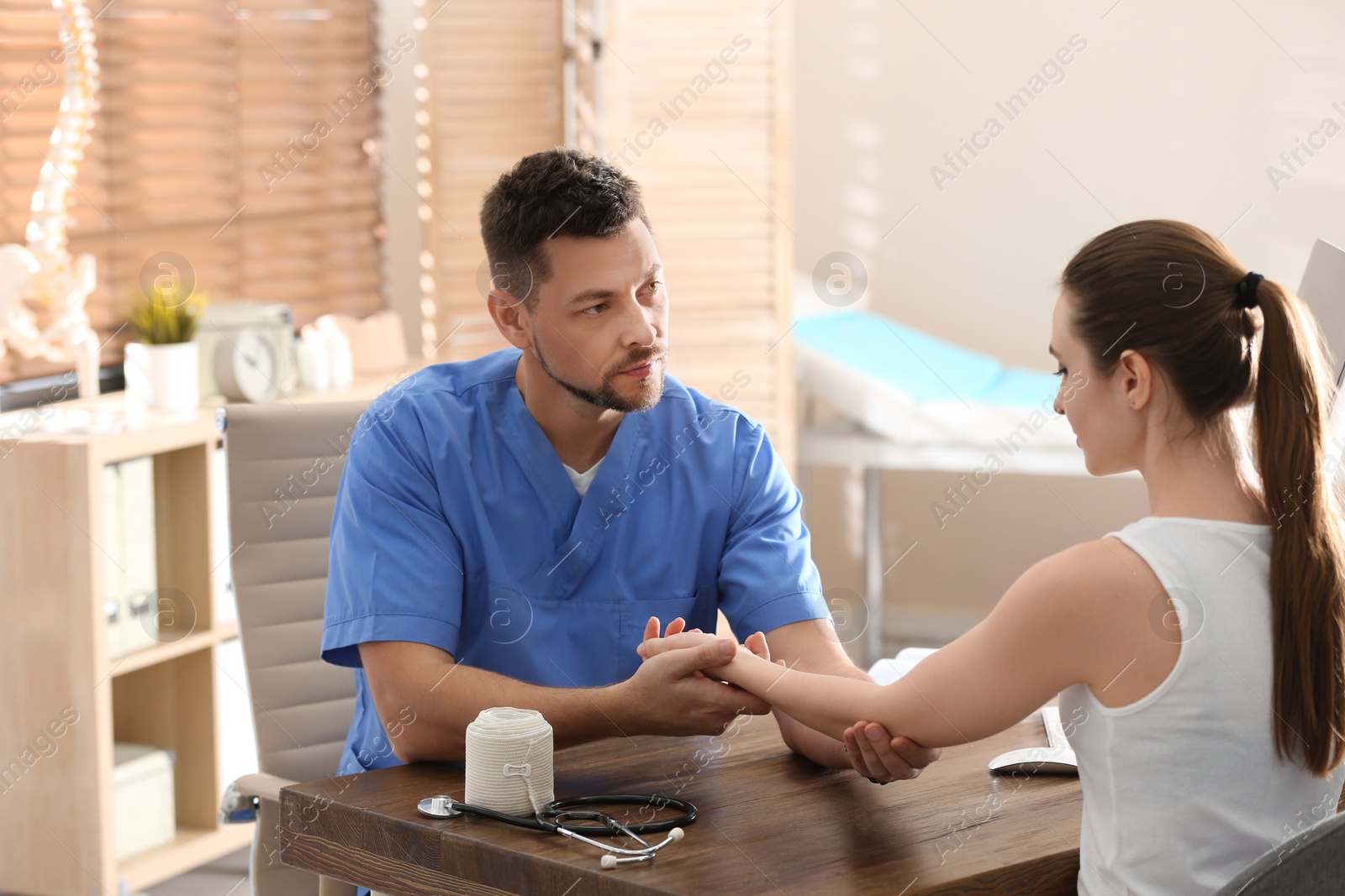 Photo of Male orthopedist examining patient with injured arm in clinic