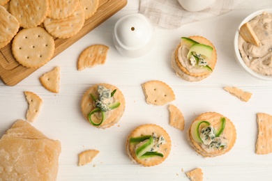 Delicious crackers with humus and cucumber on white wooden table, flat lay