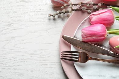 Festive Easter table setting with flowers on wooden background, above view. Space for text