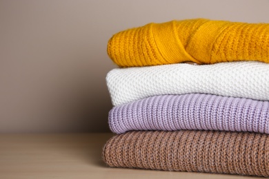 Photo of Stack of folded knitted sweaters on wooden table, closeup. Space for text